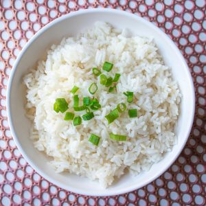 A bowl of cooked white rice garnished with green onions, perfect for culinary presentations.